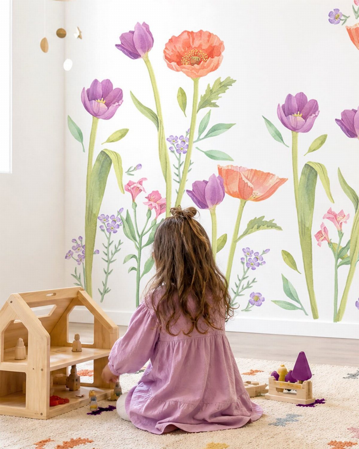 Young girl sitting before a white wall with large colorful painted flower motifs.