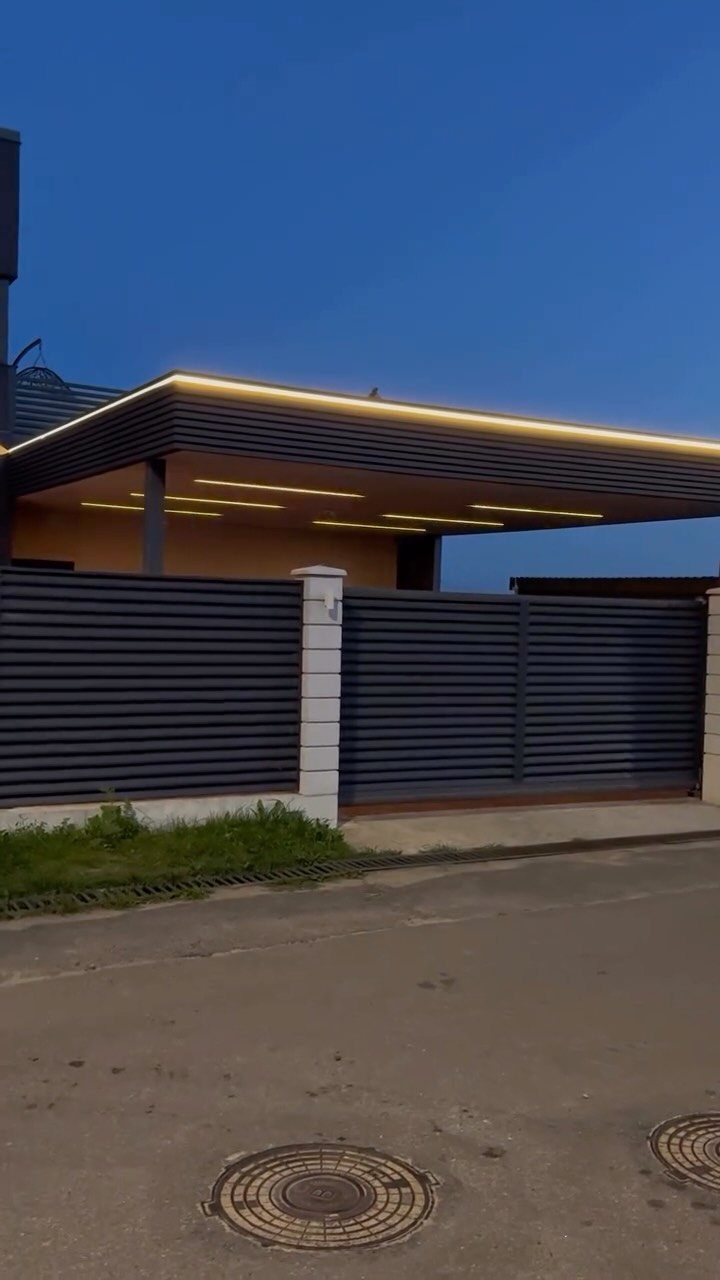 Modern carport with yellow LED ceiling lights and a dark grey slatted fence.