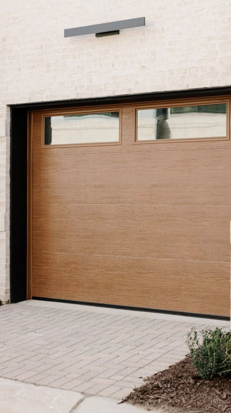 Modern brown wood-grain garage door with windows set in a white brick wall.