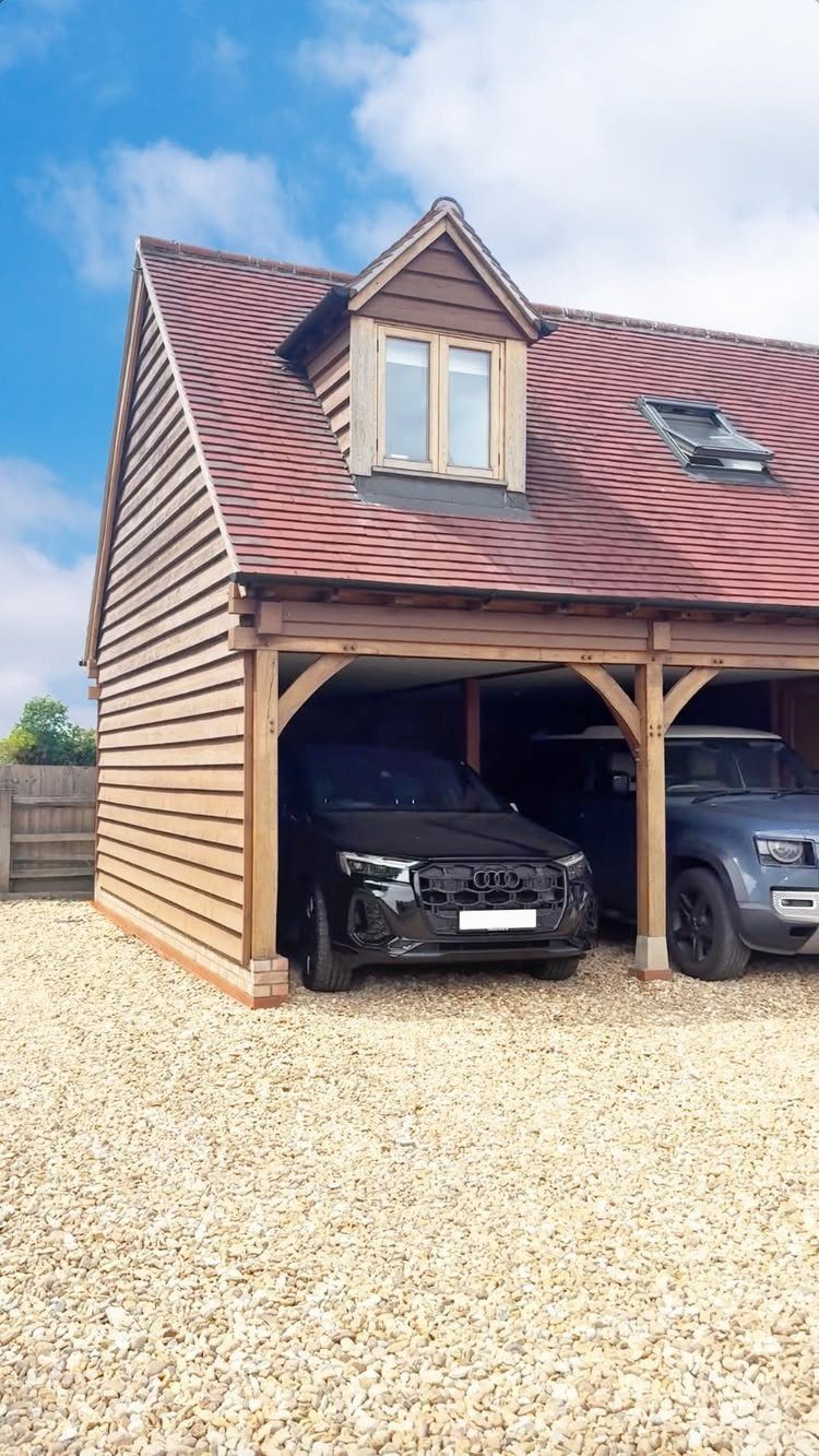 Wooden two-car garage with a red tiled roof and dormer window above parked cars.