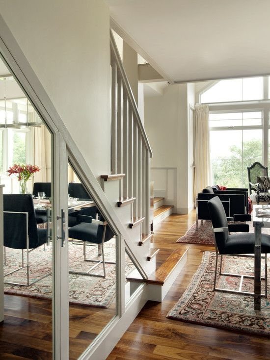White under stair storage cabinets with mirrored doors reflecting a modern dining room.