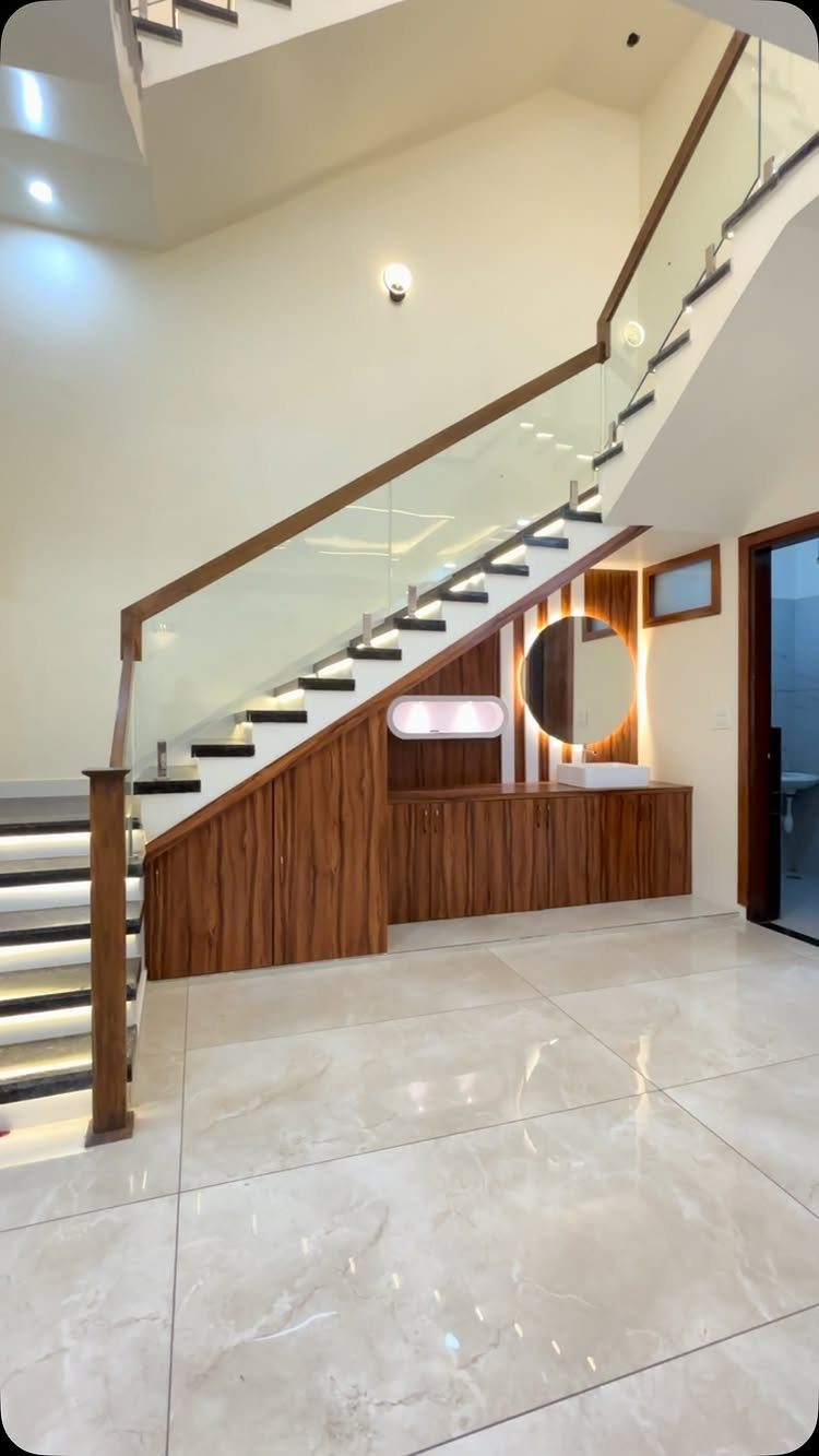 Wooden under stair vanity with a circular backlit mirror and white sink.
