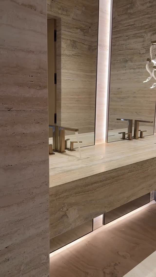 Beige travertine floating vanity with an integrated sink and gold faucets.
