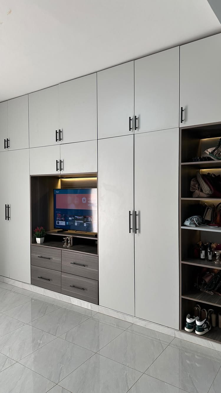 White built-in wall wardrobe unit with integrated television area and grey drawers.