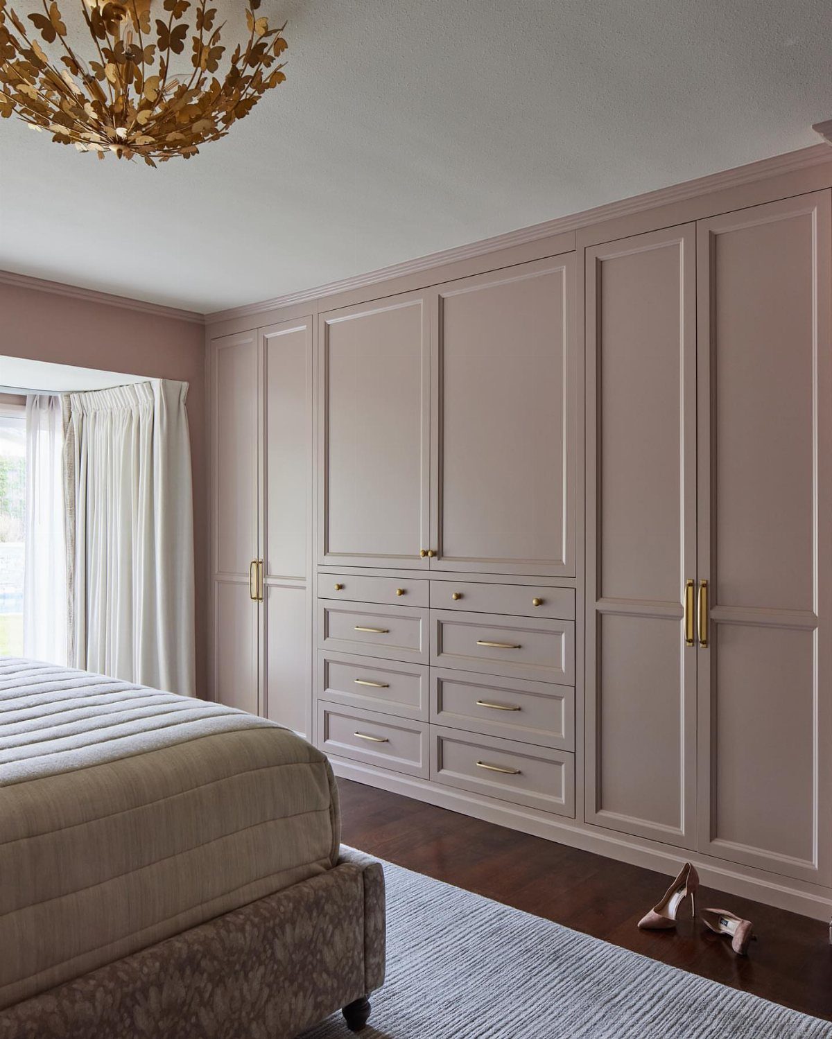 Built-in wall unit closet with mauve cabinetry and gold hardware in a bedroom.