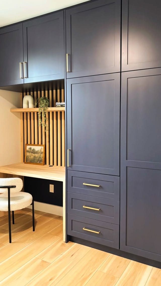 Deep blue full-wall wardrobe with integrated light wood desk and gold drawer handles.