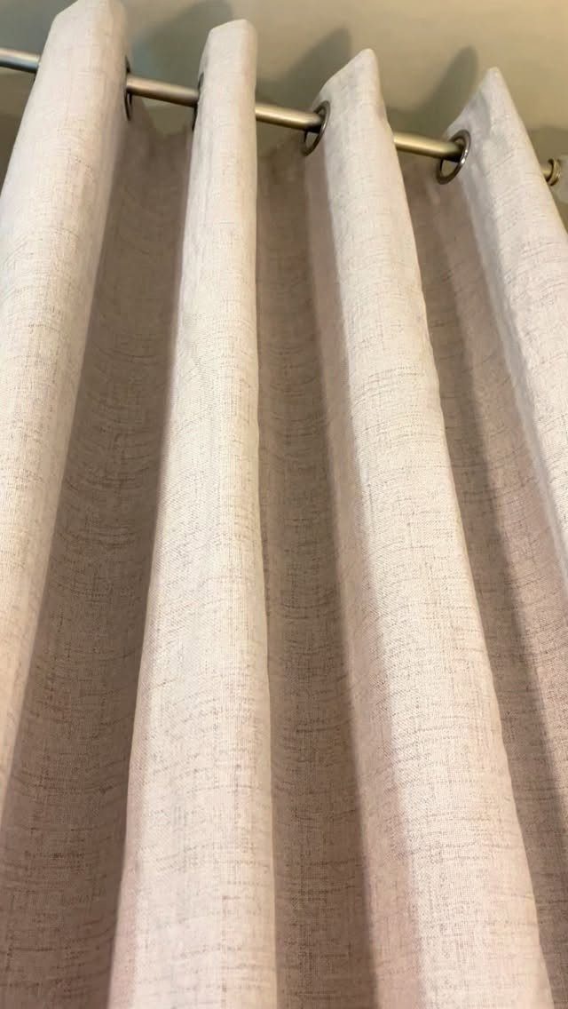 Beige textured linen curtains hanging from a silver metal rod with grommets