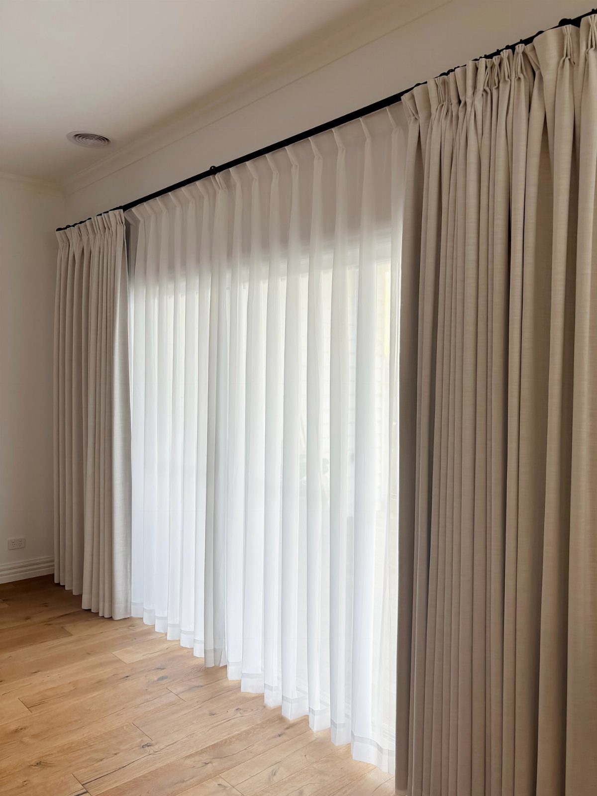 White semi-sheer curtains and beige panels hanging from a black rod in a room.
