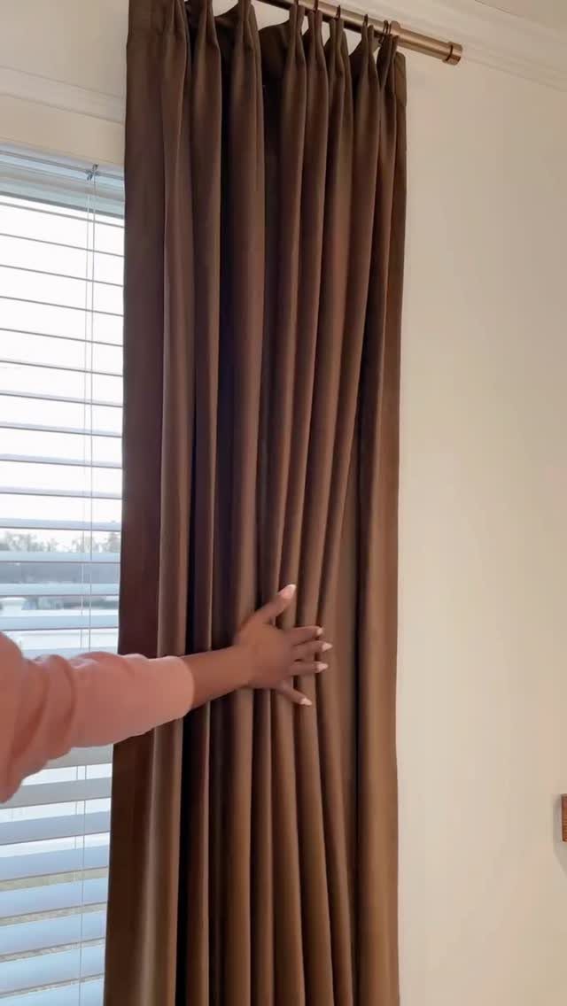 Brown velvet curtains hanging from a gold rod next to white window blinds.